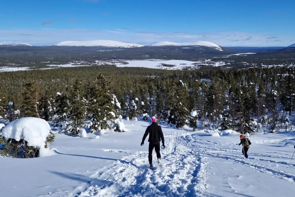 A person going down the snowy Kuertunturi fell. Many fells and a lake in the background.