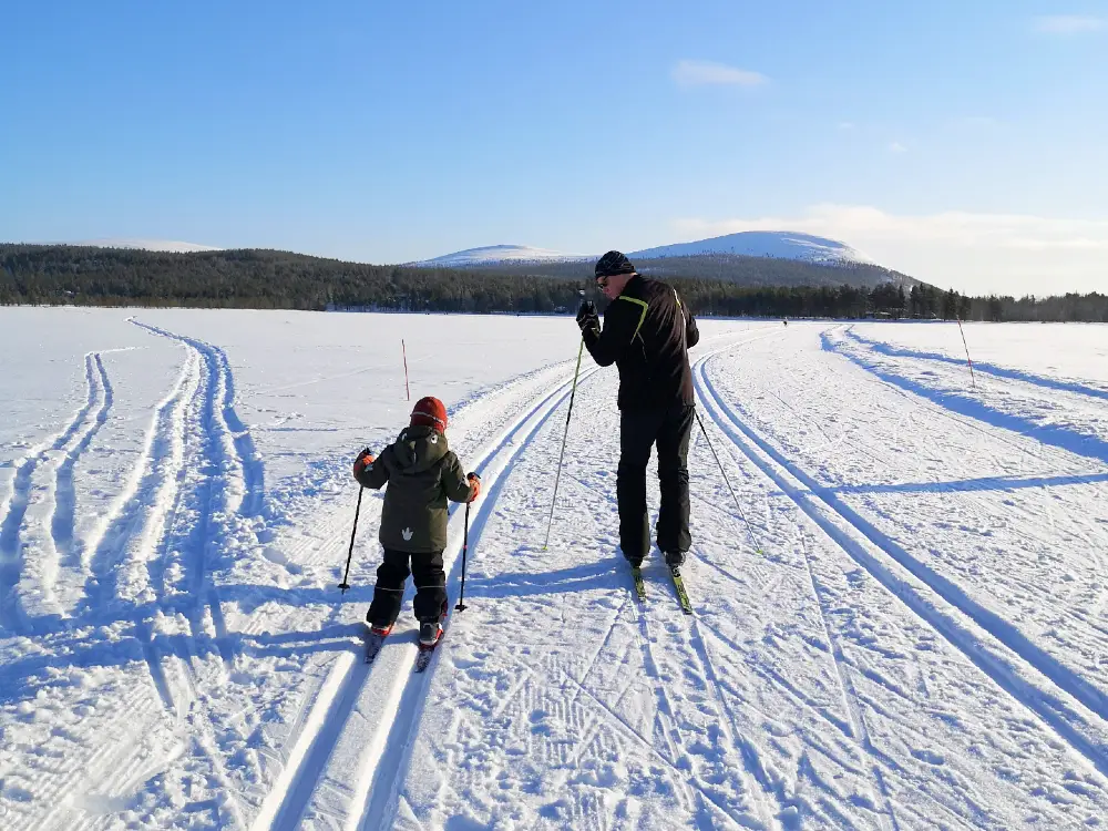 hiihto2 An elderly man skiing with a child on a frozen lake in Äksälompolo. Snowy fells on the background.