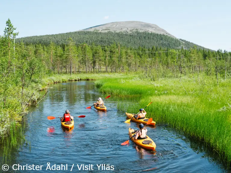 Yllas tapahtumat Outdoor Week 2023 melonta kajakki kesankijoki ChristerAdahl-VisitYllas Group of people kayaking along a calm river surrounded by green summer forest in Ylläs, Finland, with a fell rising in the background.