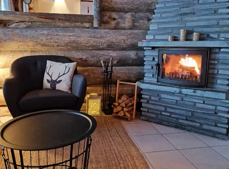 fireplace_cabin_yllas The fire burns in the fireplace of the log cabin in Ylläs. On the armchair, there’s a cushion with a reindeer image.