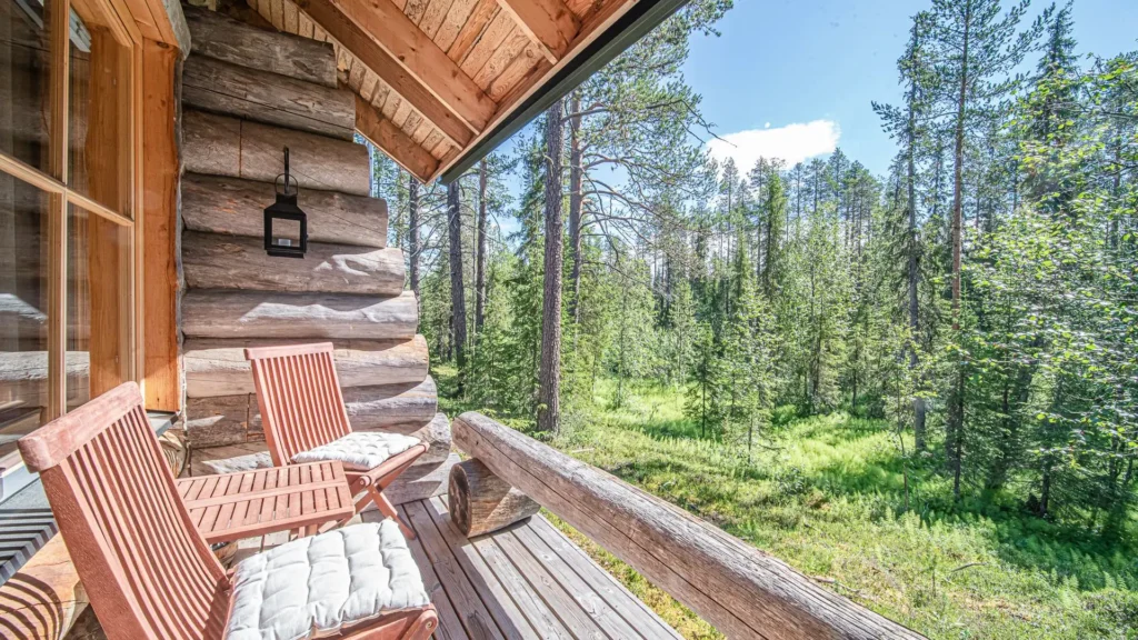 Wooden cabin terrace with two chairs overlooking a sunny forest landscape in summer.